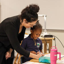 Teacher supporting student at their desk with class assignment. Student has a smile on her face.